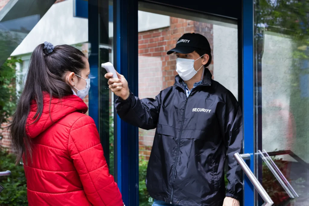 Sicherheitsmitarbeiter führt Temperaturkontrolle bei einer Besucherin als Teil der Krankenhausbewachung durch