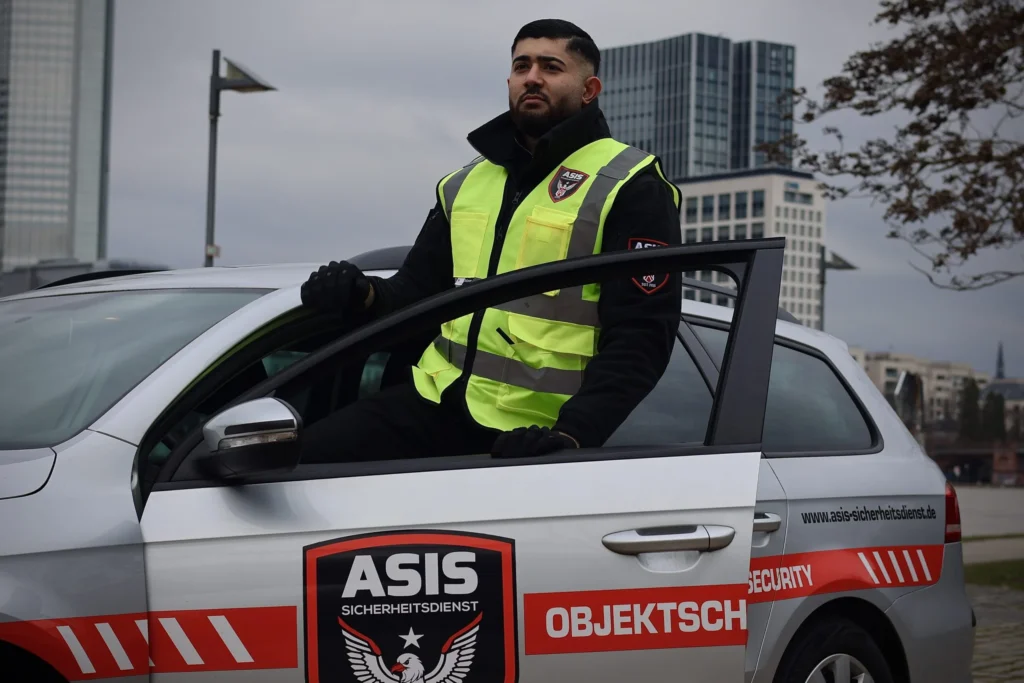 ASIS Sicherheitsmitarbeiter lehnt am Dienstfahrzeug, bereit für die Parkplatzbewachung