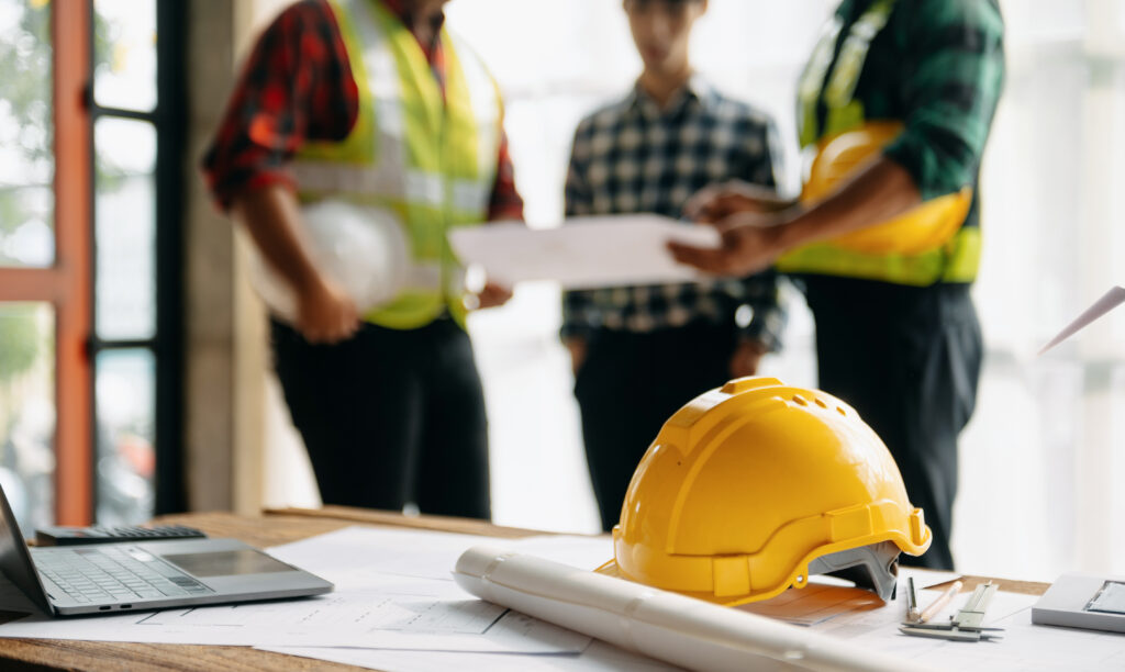 Bauleiter und ASIS Sicherheitsteam bei der Planung auf einer Baustelle mit Schutzhelm im Vordergrund