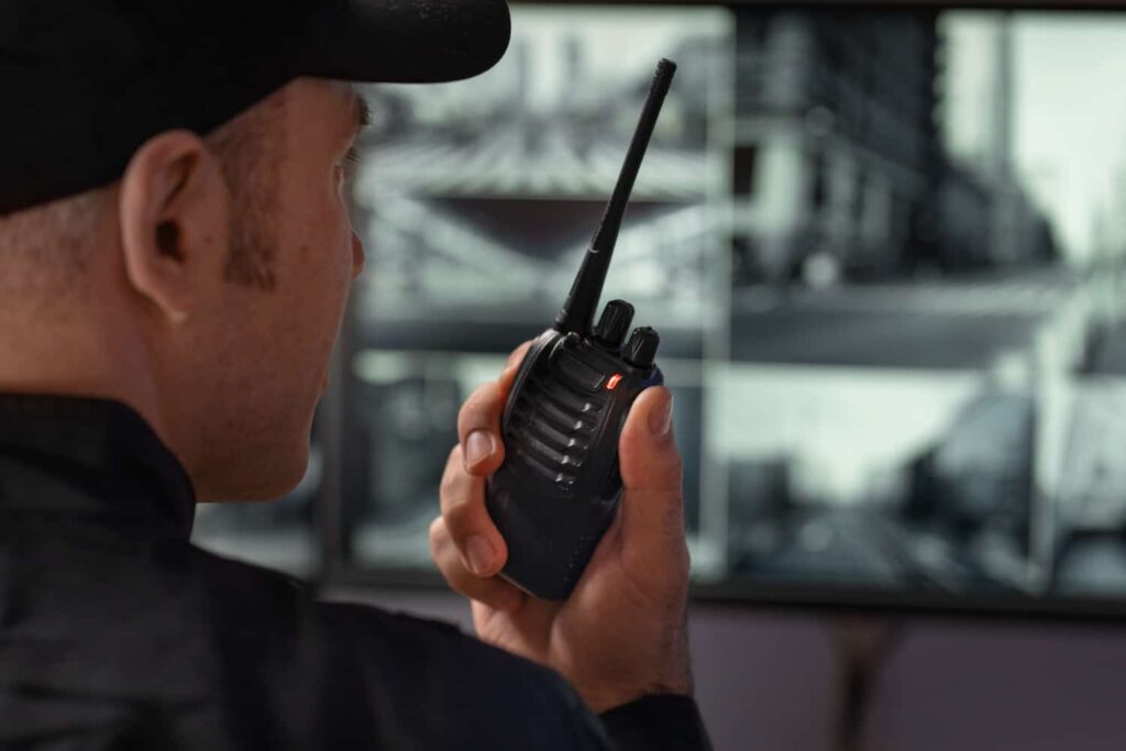 Sicherheitsdienst Landsberg am Lech – Ein Sicherheitsmitarbeiter spricht in ein Funkgerät, während er Überwachungsmonitore mit Schwarzweiß-Kameras beobachtet.